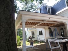 a man is working on the roof of a house that's being built in front of a large tree