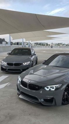 two grey cars parked next to each other in a parking lot with an awning