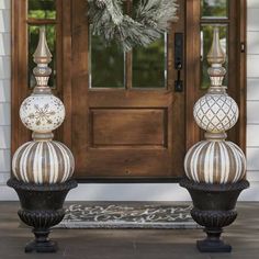 two white and black urns sitting in front of a door with a wreath on it