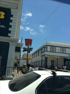 a white car parked in front of a building with people on the sidewalk and cars behind it