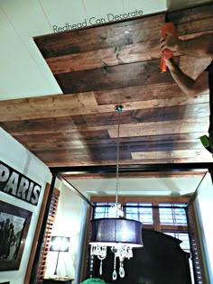 a man working on a wood ceiling in a living room with chandelier hanging from the ceiling