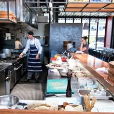 two people in a kitchen preparing food on the counter and one person standing at the stove