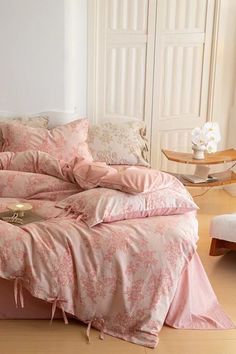 a bed with pink comforters and pillows in a room next to a window,