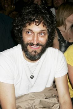 a man with curly hair and beard sitting in front of a group of other people