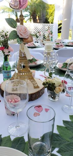 the table is set with wine glasses, plates and vases for flowers in front of the eiffel tower