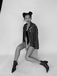 a woman sitting on top of a cement block wearing boots and a jean jacket over her shoulders