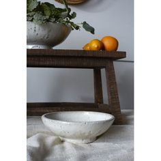 a white bowl sitting on top of a table next to oranges and a plant