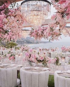 an outdoor dining area with chandelier and pink flowers on the table, along with white linen covered chairs