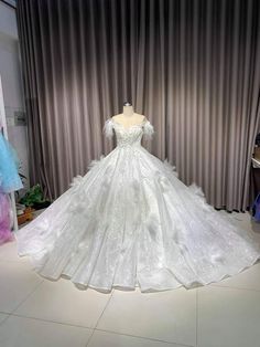 a white wedding dress on display in front of a curtained window with curtains behind it