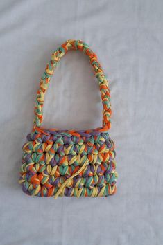 an orange, yellow and green purse sitting on top of a white sheet