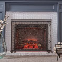 a fireplace with a fire in it next to a chair and vase filled with flowers