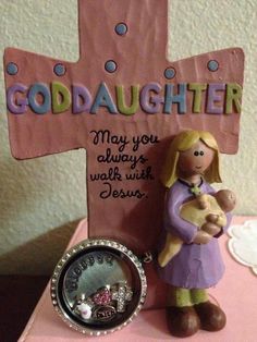 a small figurine holding a teddy bear next to a pink cross with the words goddaughter on it