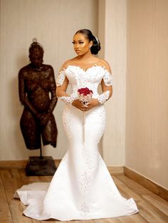 a woman in a white wedding dress standing on a wooden floor next to a statue