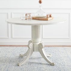 a white table sitting on top of a blue rug next to a bottle and glasses