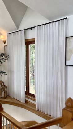 an open window with white curtains in a living room next to a bannister