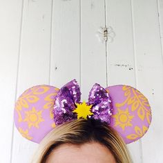 a close up of a person wearing a minnie mouse ears headband with purple and yellow decorations