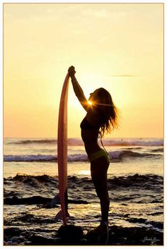 a woman holding a surfboard while standing in the ocean at sunset or sunrise time