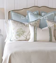 a bed with blue and white pillows on top of it's headboard next to a lamp