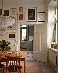 a dining room table with chairs and pictures on the wall above it, in front of a doorway