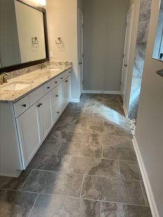 a large bathroom with gray tile floors and white cabinets