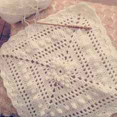 a white crocheted doily on a wooden table with yarn and knitting needles