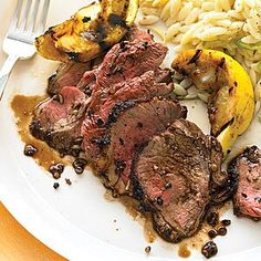 a white plate topped with meat and veggies next to pasta on a table