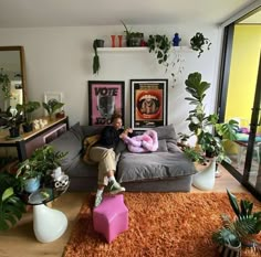 a man sitting on top of a couch in a living room filled with potted plants