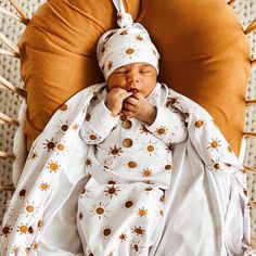 a baby laying on top of a brown pillow next to a white and orange pillow