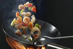 shrimp and vegetable stir frying in a wok over an open flame