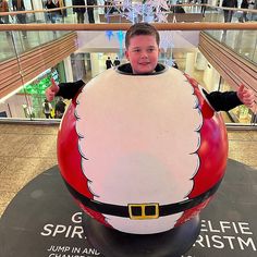 a young boy standing in front of a giant santa clause egg at an airport terminal