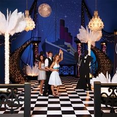 three people standing on a checkered floor in front of a stage with lights and chandeliers