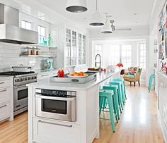 a kitchen with lots of white cabinets and blue stools next to an island in the middle