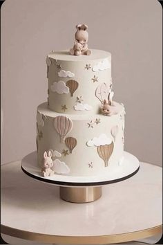 a three tiered cake decorated with hot air balloons and bunnies is on a table