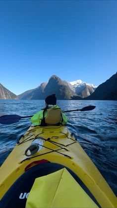 a person in a kayak paddling on the water with mountains in the background