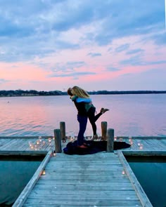 a woman standing on top of a pier next to the ocean at sunset with her leg in the air