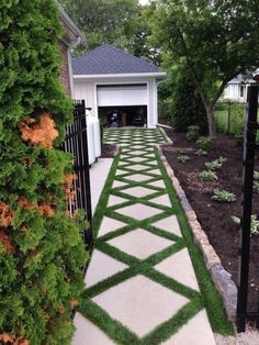 a driveway with grass growing on it and a black gate in the middle, leading to a garage