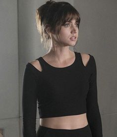 a woman in black top and pants standing next to a wall with her hands on her hips