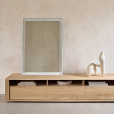 a white vase sitting on top of a wooden table next to a mirror and shelf