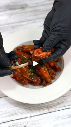 two hands in black gloves are picking up food from a white plate