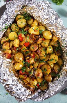 cooked potatoes in foil on a plate with parsley sprigs and tomatoes around the edges