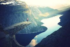 a person standing on the edge of a cliff overlooking a body of water and mountains