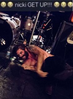 a shirtless man laying on the ground next to a set of drums in front of him