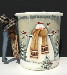 a ceramic mug with a snowman and birds painted on the side, sitting next to a christmas ornament