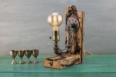 an old fashioned light bulb sitting on top of a piece of wood next to three goblets