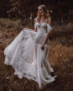 a woman in a white dress is walking through the grass with her hands on her hips