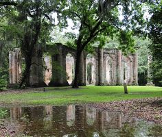 an old ruin with trees and water in the foreground