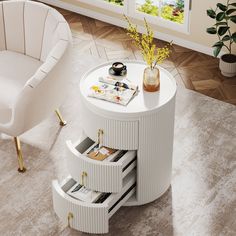 a white round table with drawers on the bottom and two chairs in the middle, next to a potted plant