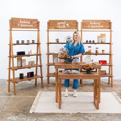 a woman standing in front of two wooden shelves with baked goods on them and holding a tray