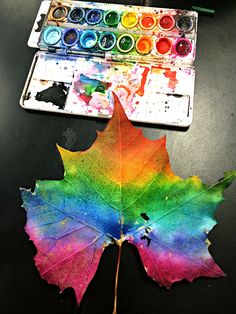 a colorful leaf sitting on top of a table next to watercolors and a paintbrush