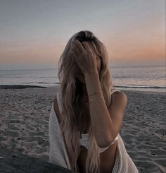 a woman sitting on top of a wooden bench next to the ocean with her head in her hands